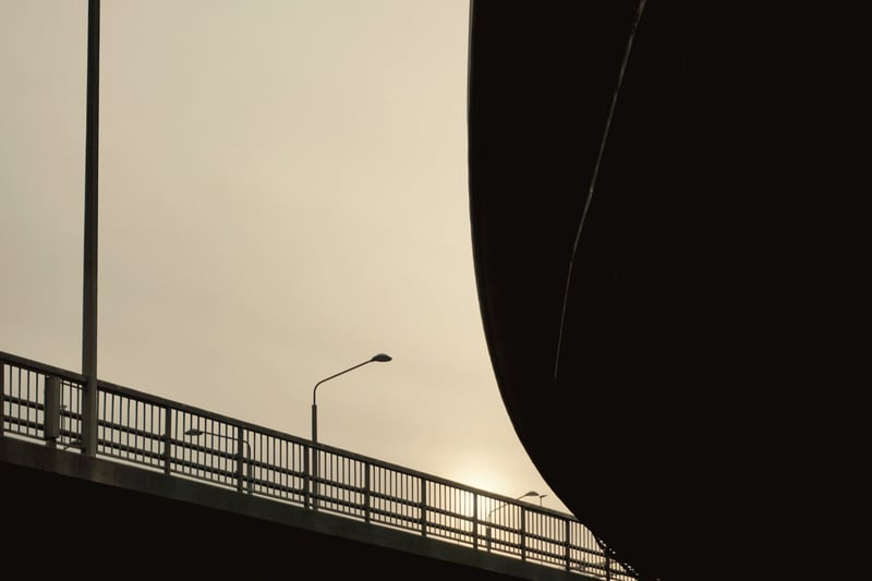 Bridge railing and street lamps under a curving concrete underside at dusk, Stockholm