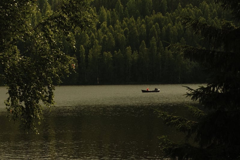 A rowing boat on a still Finnish lake below dark forest