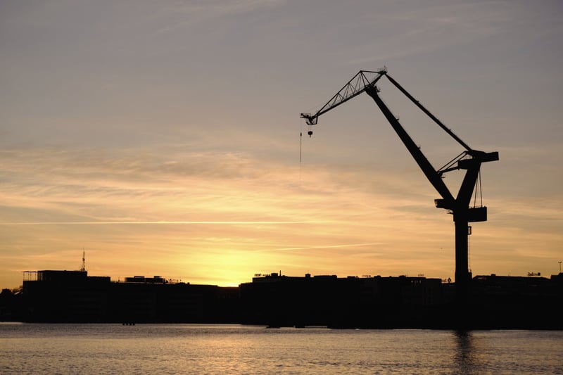 Harbour cranes silhouetted against a low Nordic sun