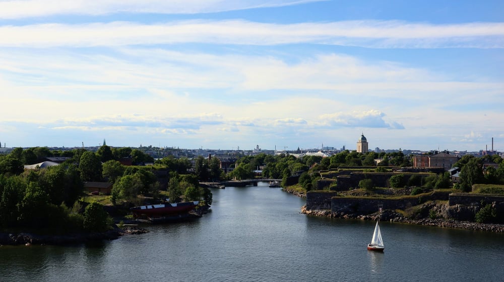 Kanal mellan öarna vid Sveaborg med en segelbåt, Helsingfors skyline och katedralkupol vid horisonten