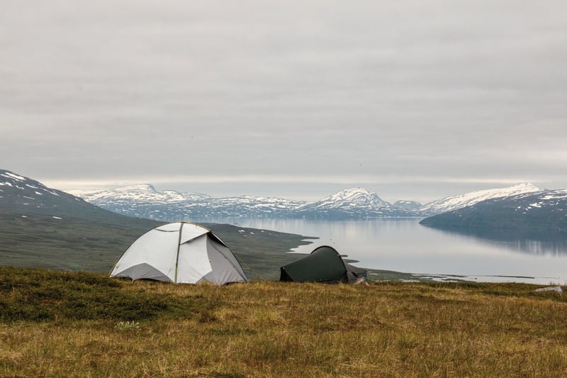 Två tält uppslagna på en grön bergsrygg ovanför fjord och toppar